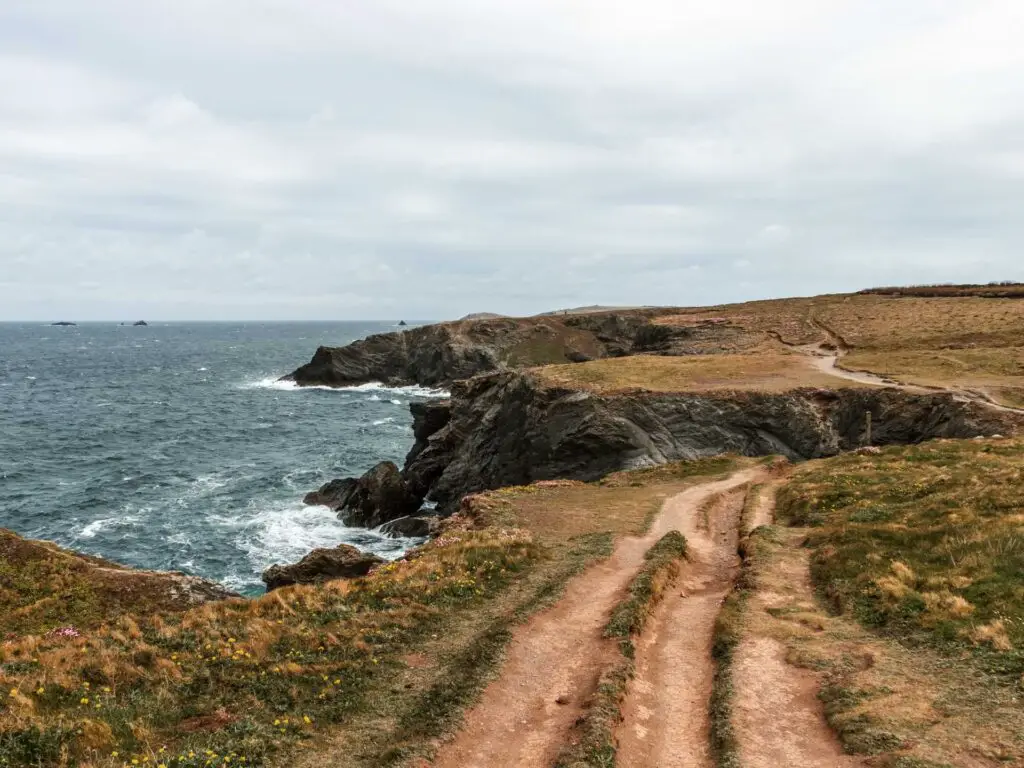 A dirt trail running along the cliff top with a view all down the coastline on the walk from Porthcothan.