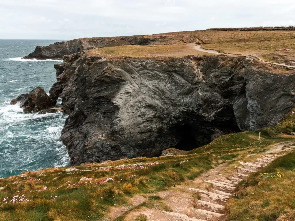 Steps leading downhill with black rock cliffs on the other side on the walk to Treyarnon in Cornwall. The seas is crashing into the cliffs on the left.