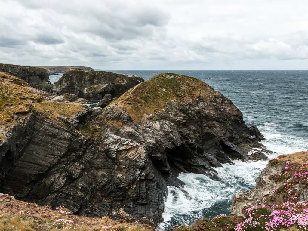 The hilly rugged coast of Cornwall with the sea crashing into into it.