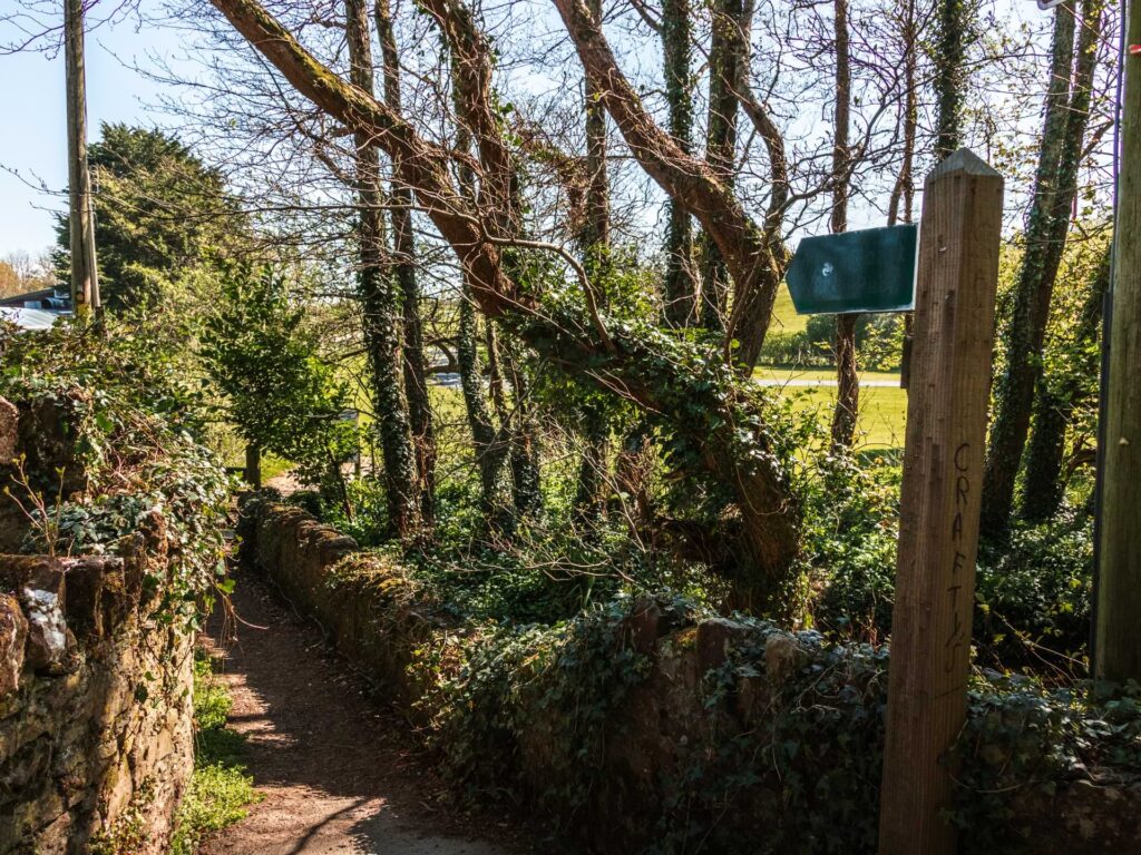 The walking trail with a low brick wall on the right of it and a wooden signpost pointing along it.