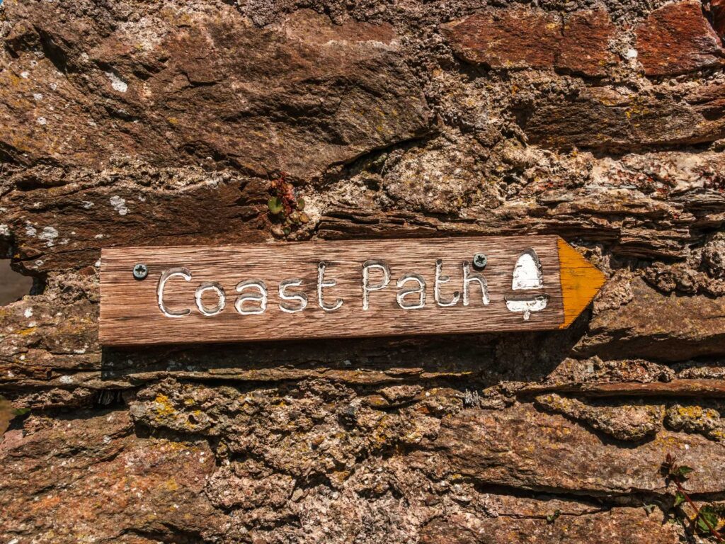 Wooden coast path signage screwed to a brick wall.