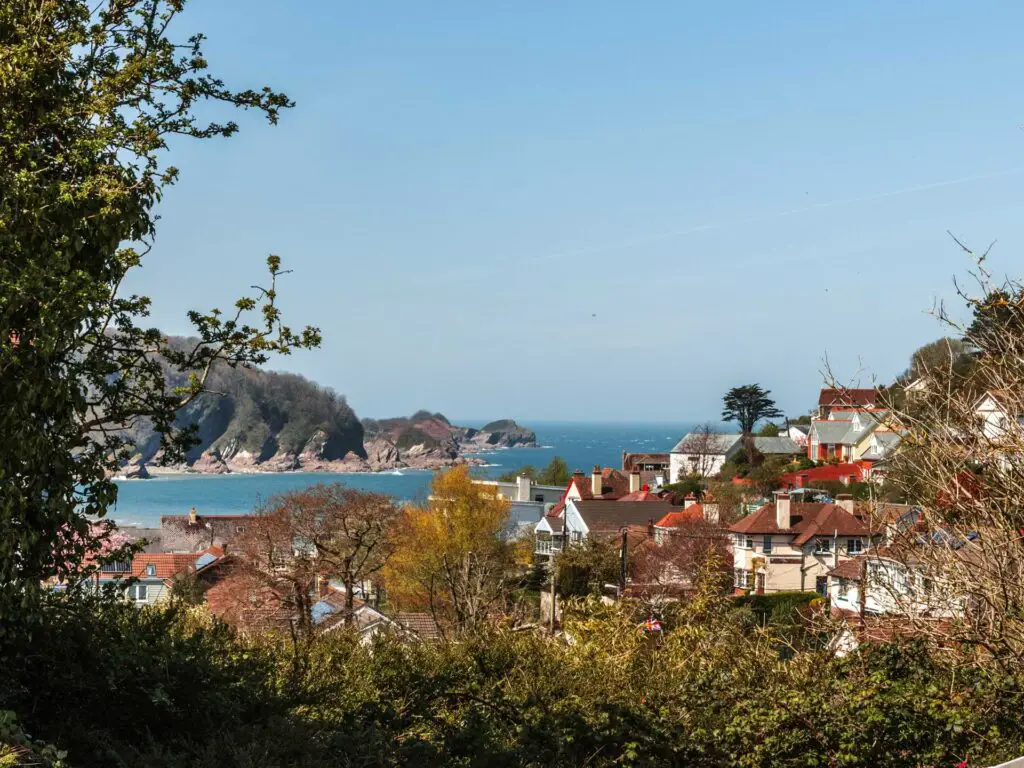 A view to the houses and rooftops of Combe Martin on the walk from Ilfracombe and Watermouth. The blue sea is visible past the houses with the rugged coastline on the other side.