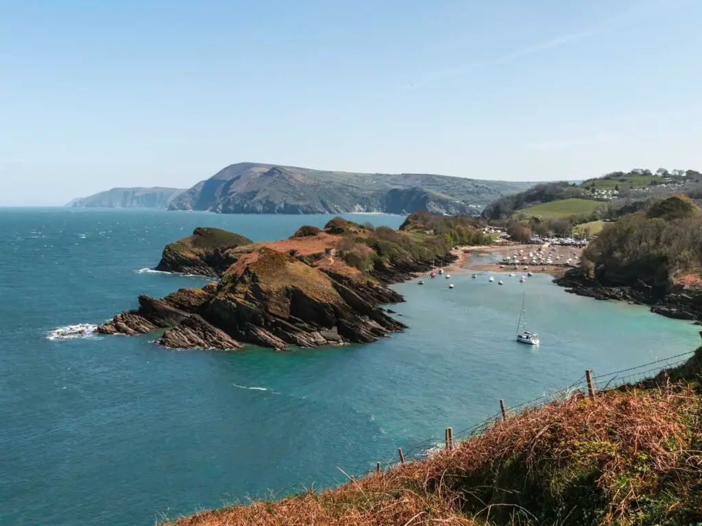 A view down to the peninsula of watermouth and the beach, on the walk from Ilfracombe. There are a few boats in the water.