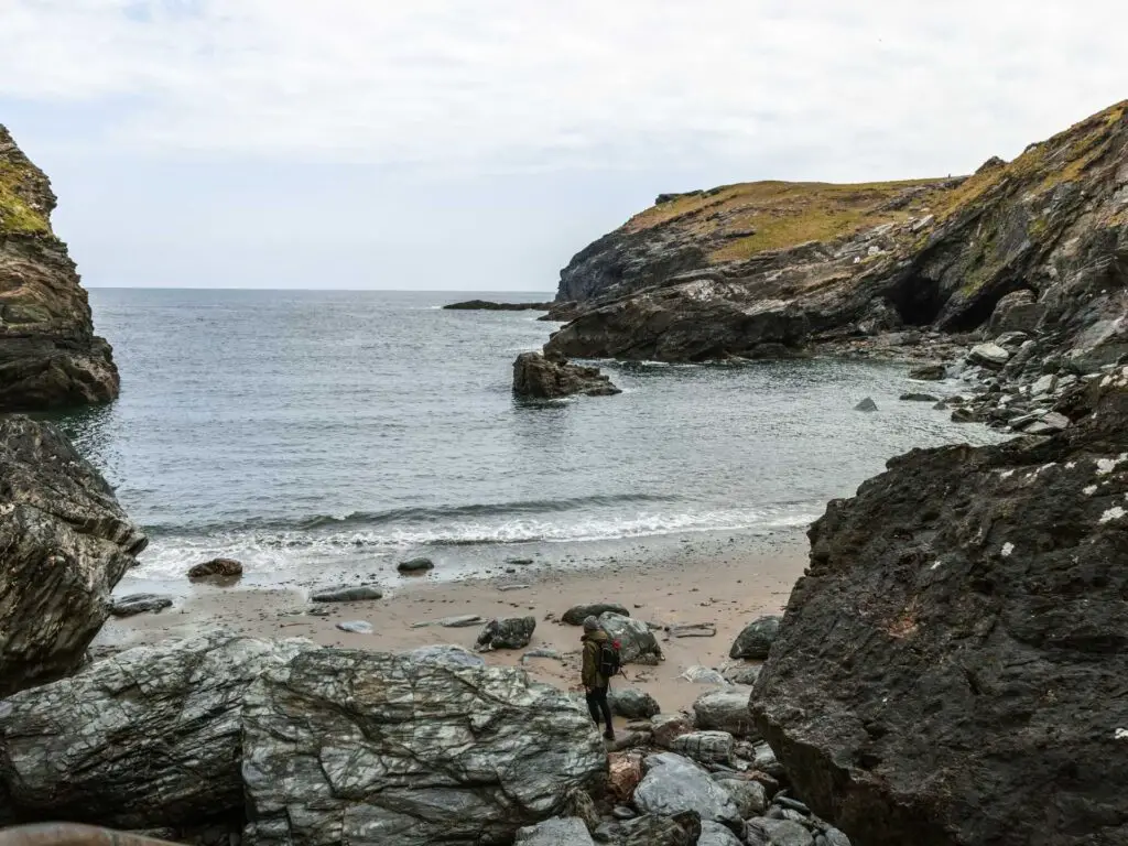 Rocks leading down to a sandy beach surrounded by cliffs on the Tintagel walk. there is a man standing on the beach.