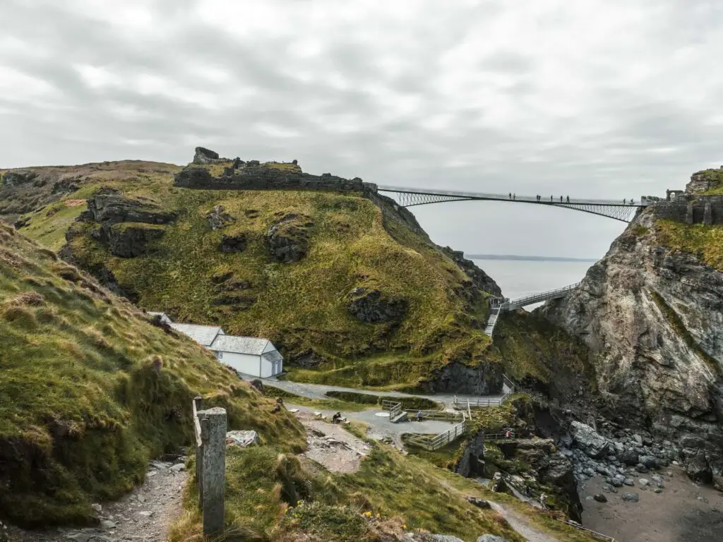 Rugged grass covered hills and cliffs on the coastal walk from Tintagel to Bossiney. There is a high bridge leading between two hills.