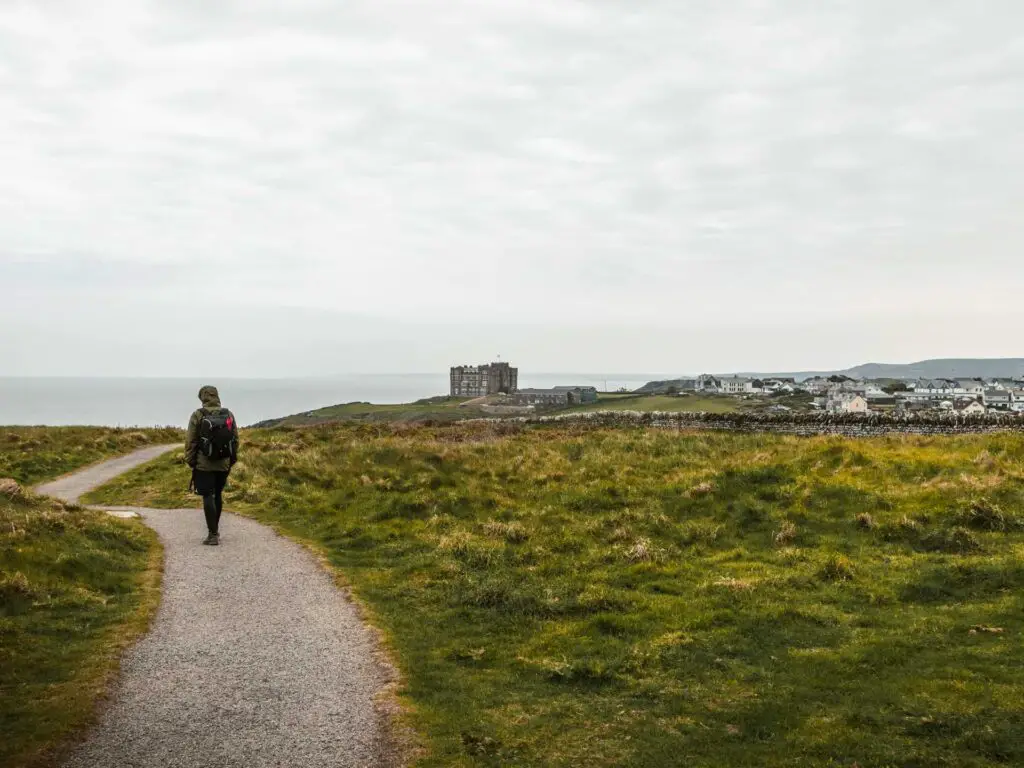 A walking trail through the overgrown grass and the sea and Tintagel village in the distance. 