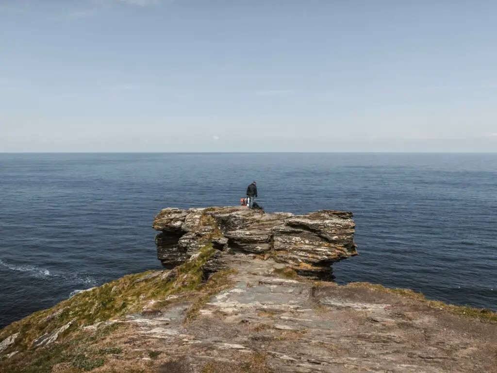 A man standing at the tip of the cliff of Barres nose, with the blue sea behind.