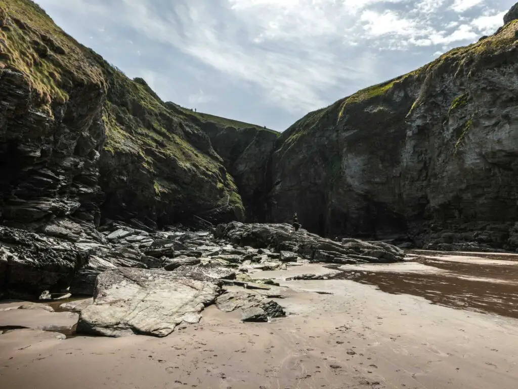 Sand leading to slabs of rock, enclosed on the other side by steep craggy cliffs on Bossiney Bay.