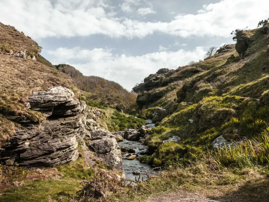 A small stream at the bottom of a valley and rugged hills on either side of it.