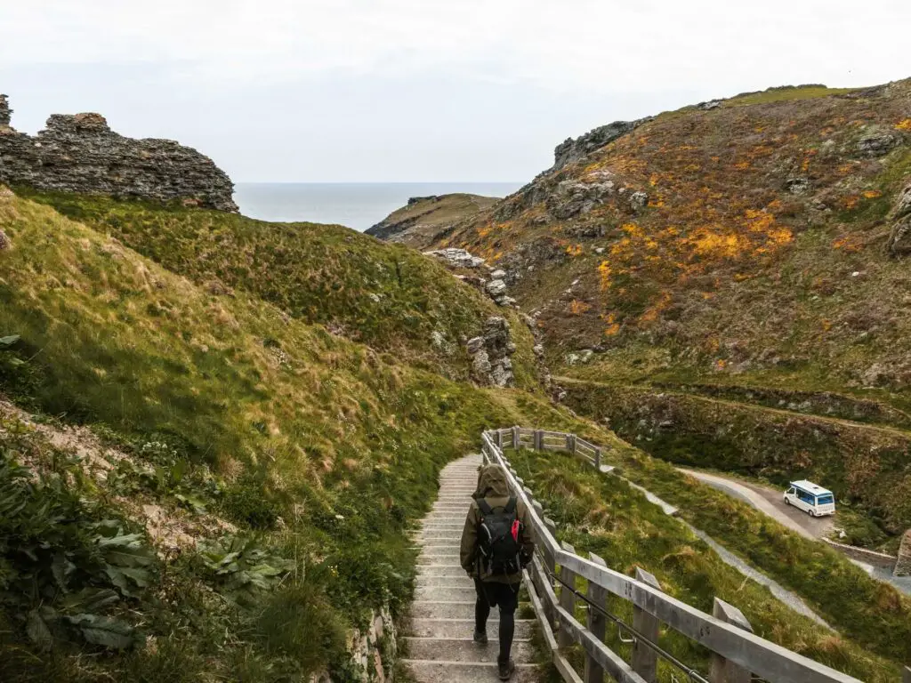 A man walking down some steps with a wooden fence on the right and green grass covered hill on the left.