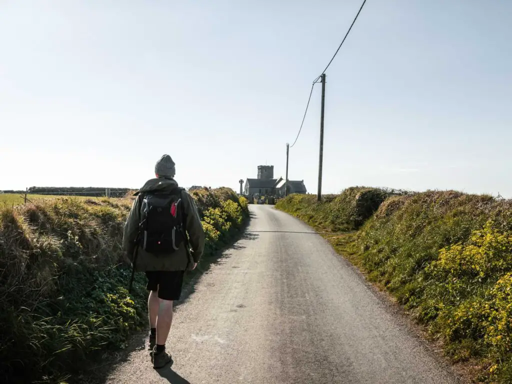 A man walking on a road with green hedges on either side.