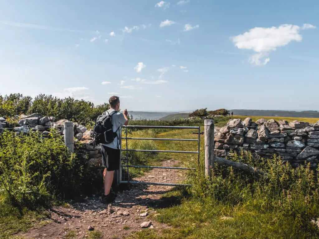 A man walking through a metal gate through the stone wall.