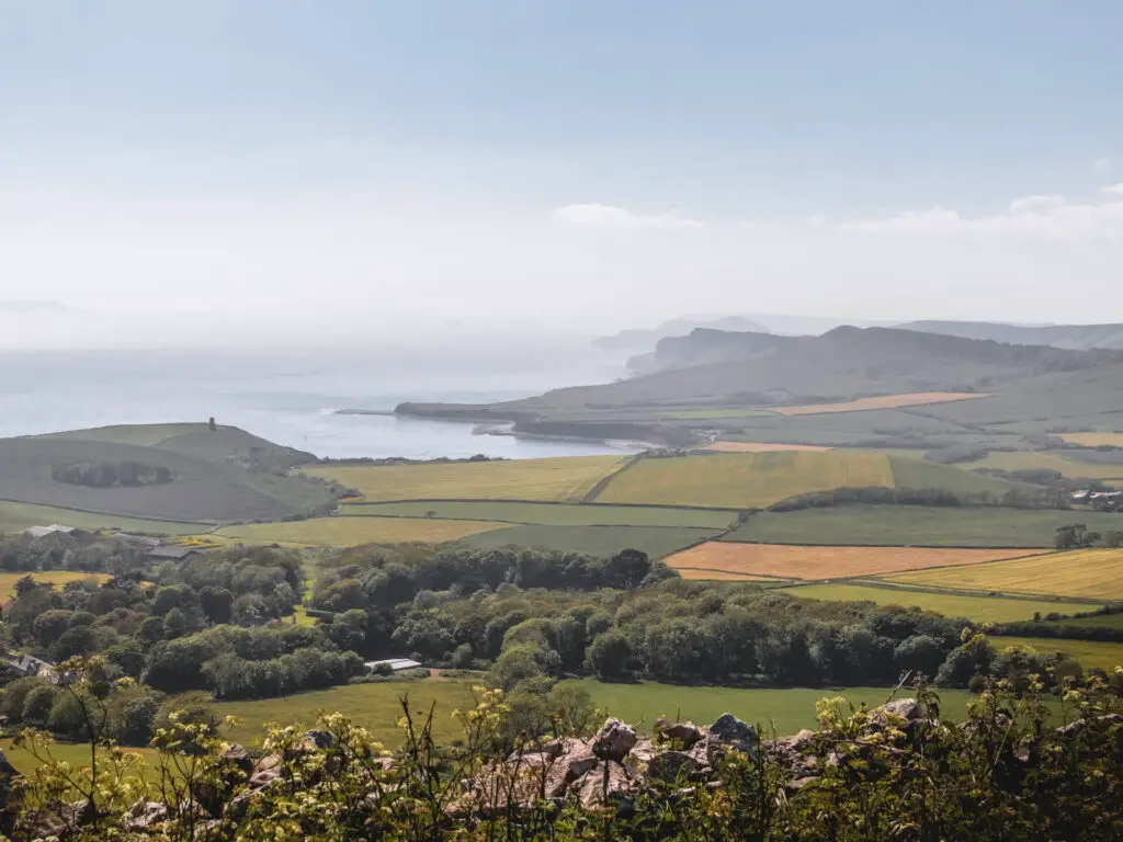 A view across the the fields and hills to the coastline on the Kimmeridge circular walk. The mist is settling across some of the hilly coastline in the distance. 