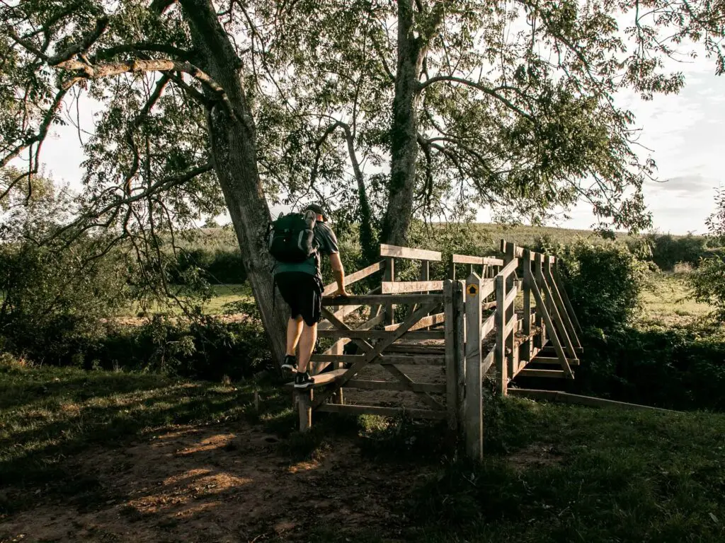 A man climbing over a wooden style to get onto the wooden bridge on the circular walk from Balcombe to the Ouse Valley viaduct. 