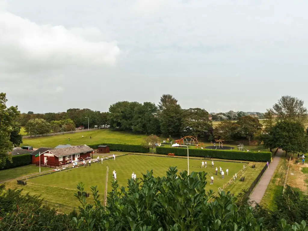 Looking down to the bowls green with  people wearing white playing on it.