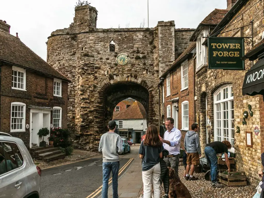 The stone arch Landgate in Rye. A road is running under it, with people mingling on the side of the road.