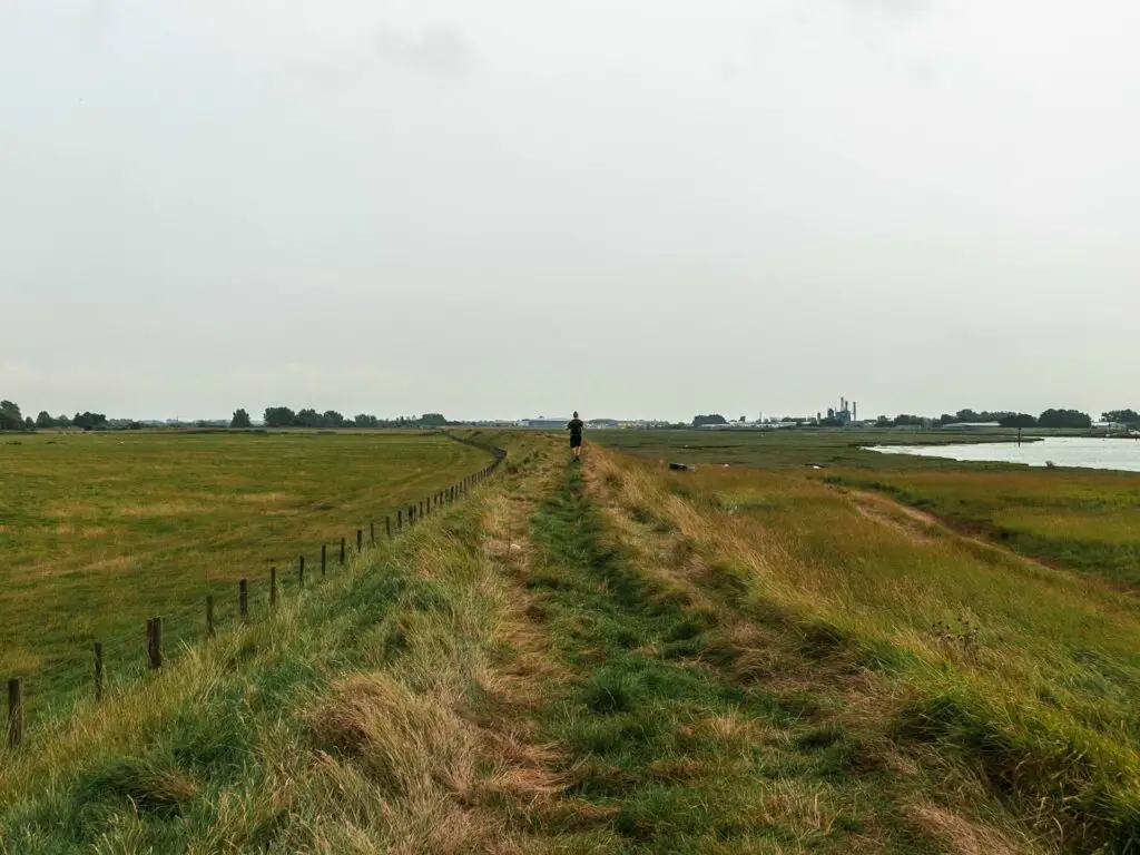 The green grass ridge trail with a man walking along it in the distance.