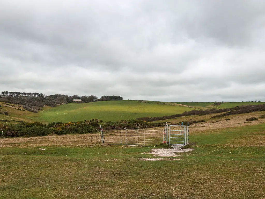 The undulating grass covered fields. There is a metal gate, and wires separating the fields.