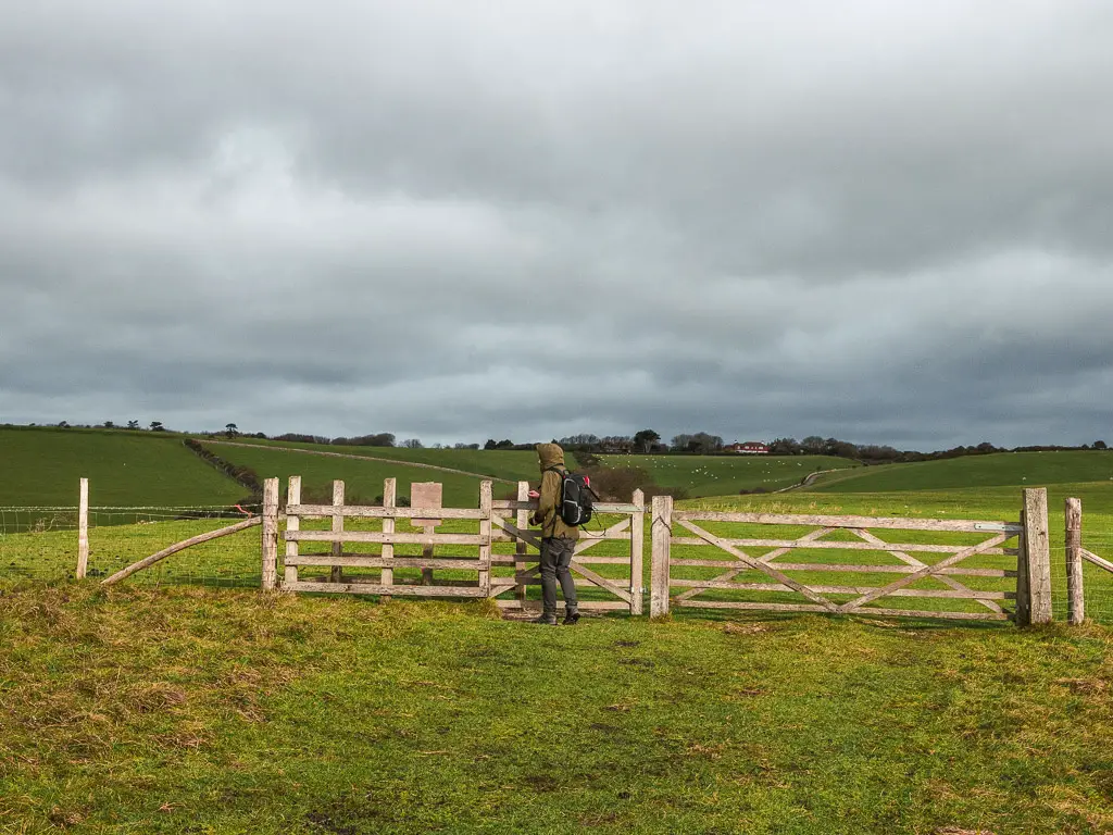 A man walking through a wooden gate into the next field on the walk away from Birling Gap, towards Friston Forest.