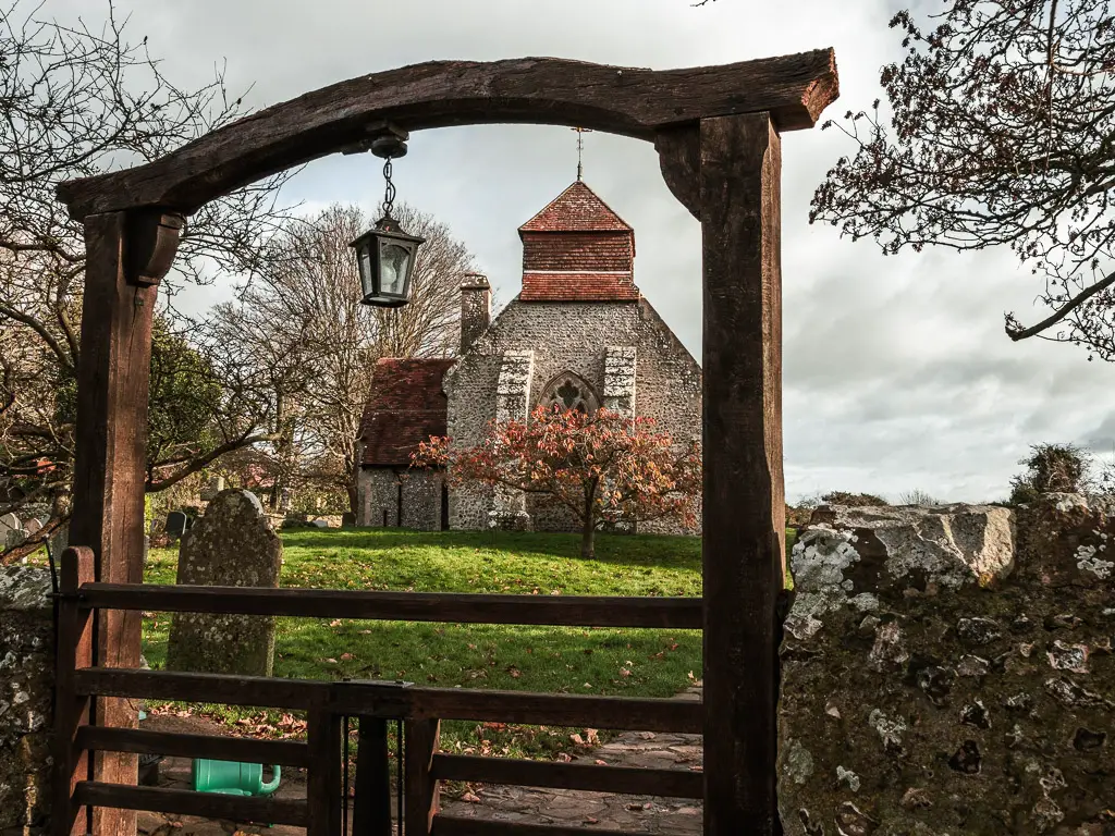 Church of St Mary viewed through the wooden arch on the walk to Friston Forest, from Birling Gap. There is a lantern hanging from the arch.