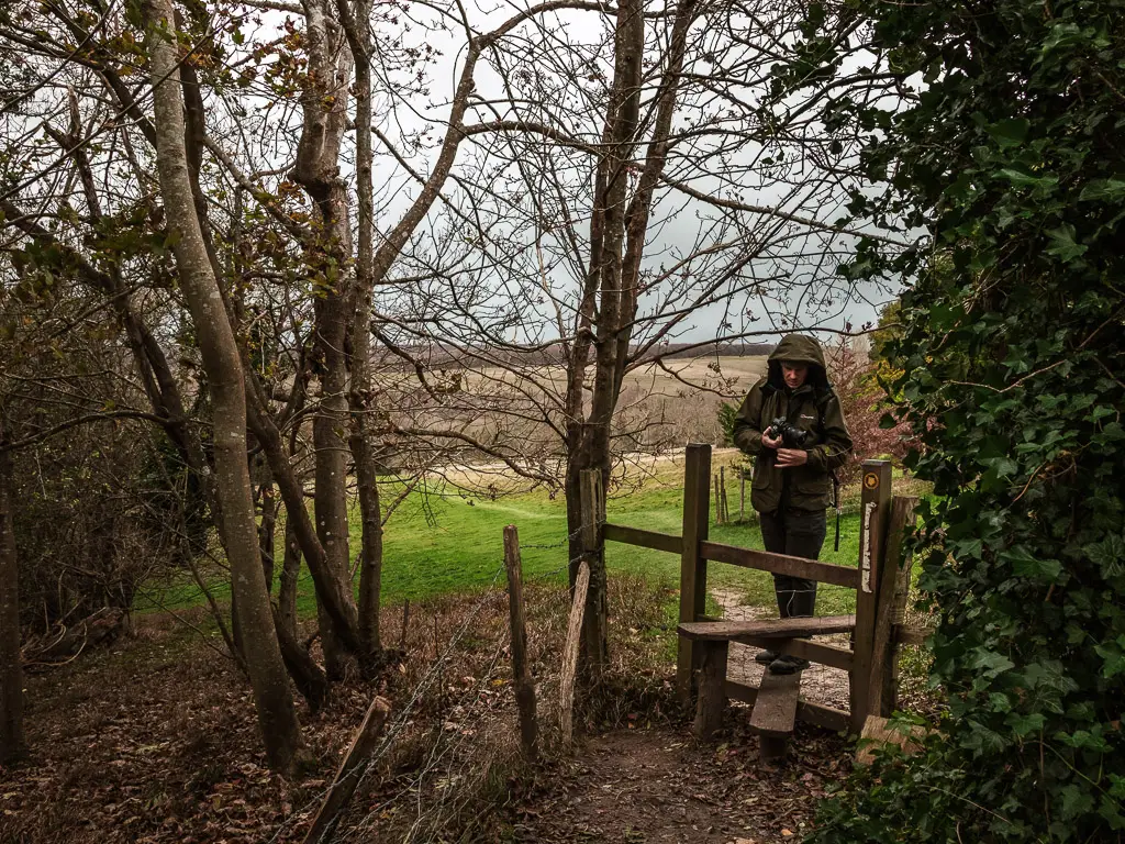 A man standing on a stile, with a field on the other side.