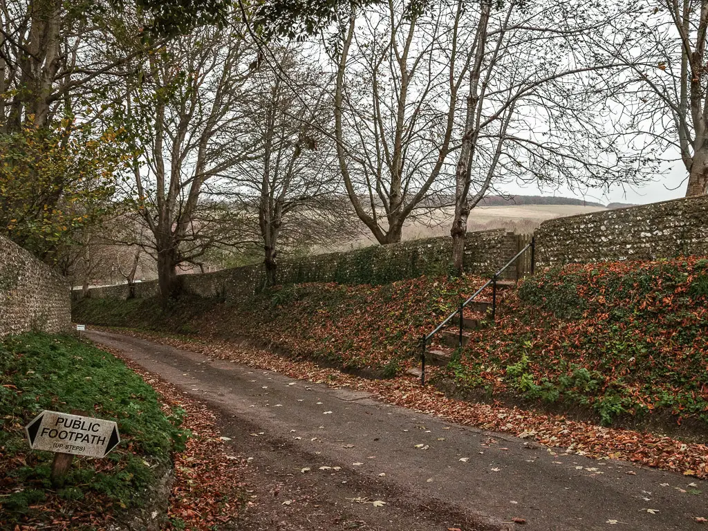 Steps next to the road, leading up to a brick wall surrounding a field. 