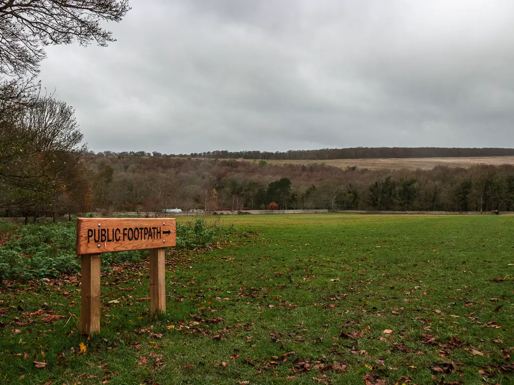 A large grass covered field, with a small sign saying 'public footpath'.