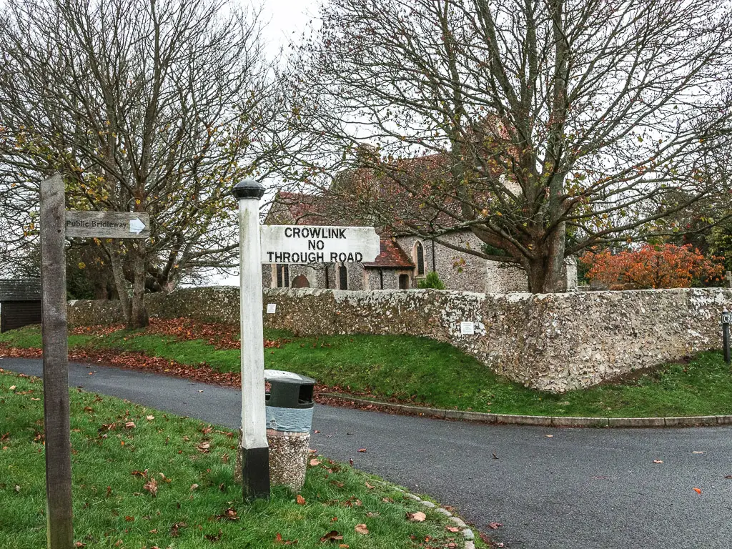 A white signpost on the road, with St Mary's Church behind on the walk back to Birling Gap from Friston Forest.