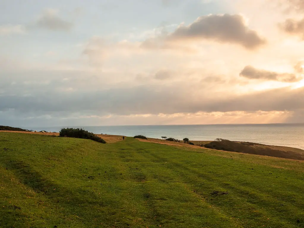 A walk along a grass track across the clifftop field near Birling Gap. The sun is low in the sky creating and orange glow.