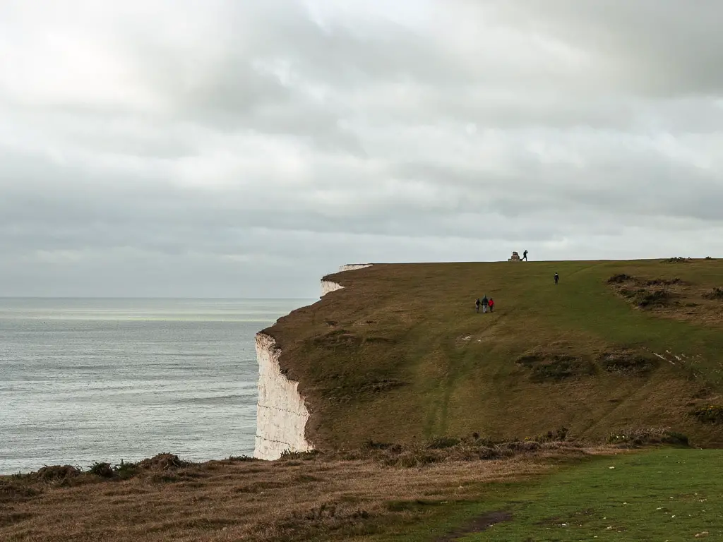 The grassy clifftop of the Seven Sisters near Birling Gap, with some people visible on a walk up the hill.