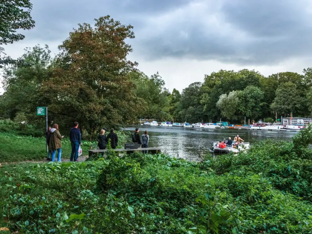 looking across the green bushes to people waiting in line to cacti the ferry boat across the River Thames.