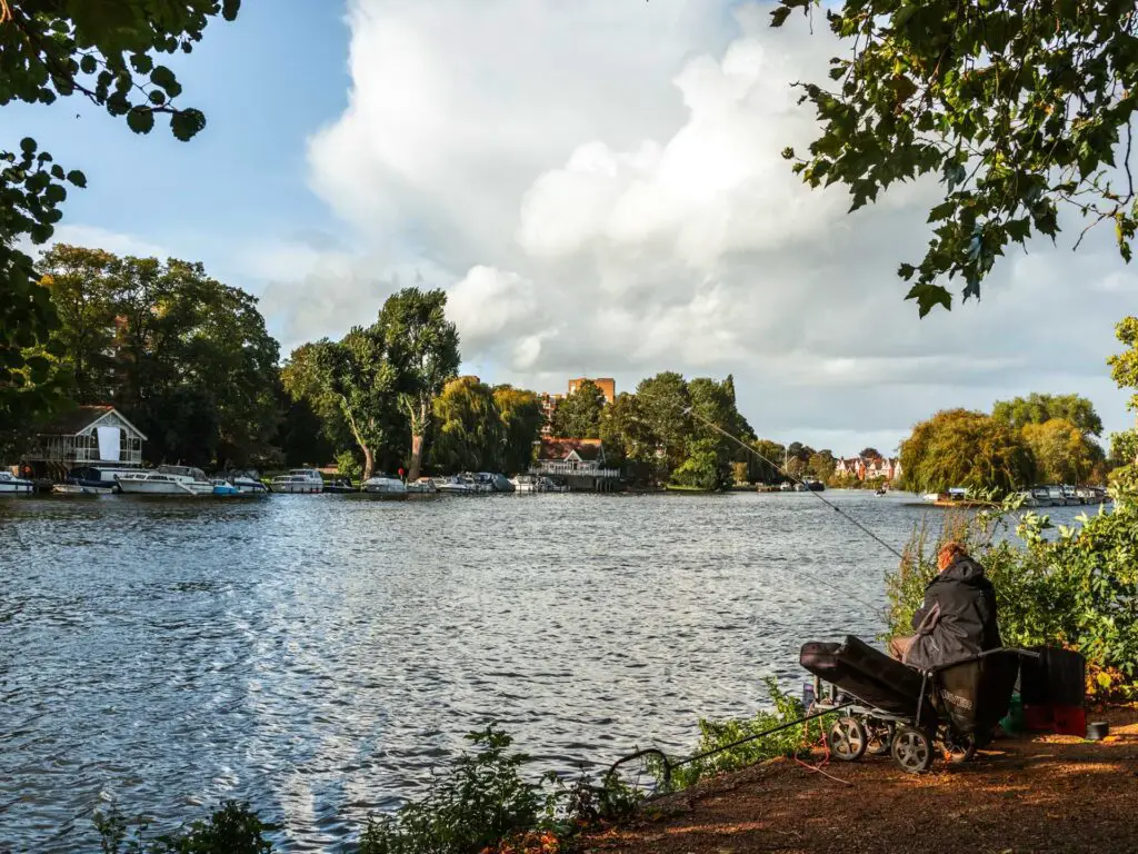 A man sitting on the bank of the River Thames fishing, on the walk into Kingston.