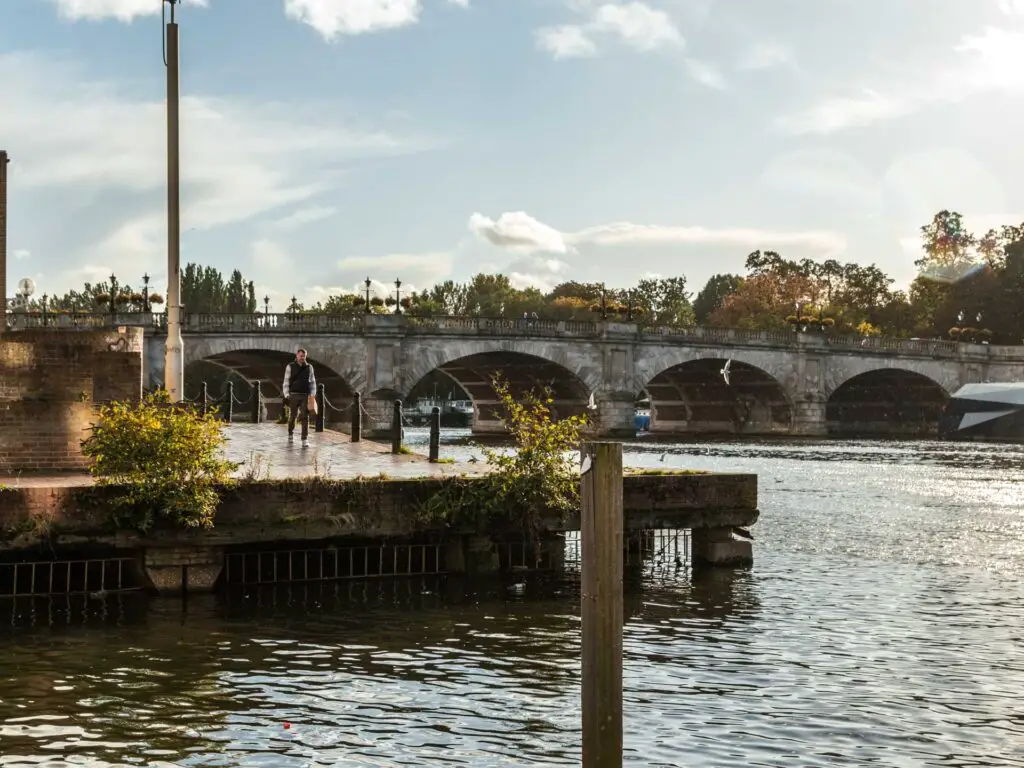Looking across the River Thames to a platform and Kingston bridge on the walk from Richmond to Hampton Court and Bushy park. There is a man walking on the platform.