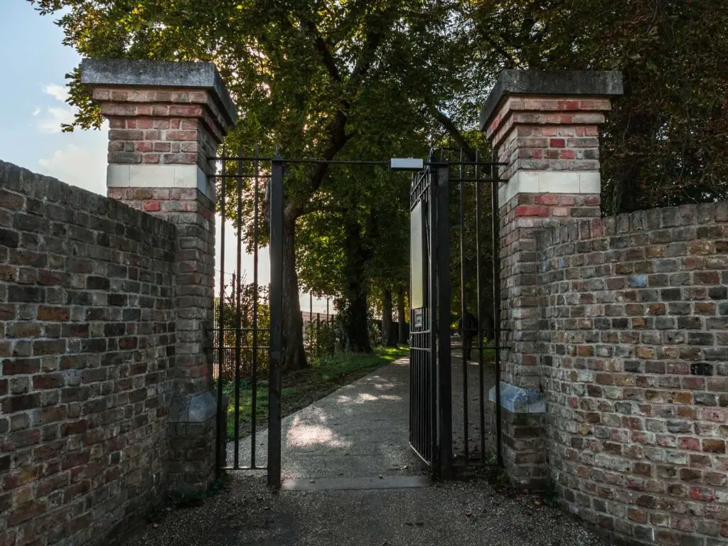 A metal gate with a brick wall on wither side on the walk into bushy park.