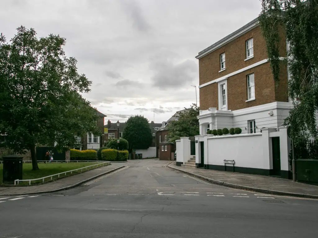 A road with a house and white wall on the right and some houses ahead.