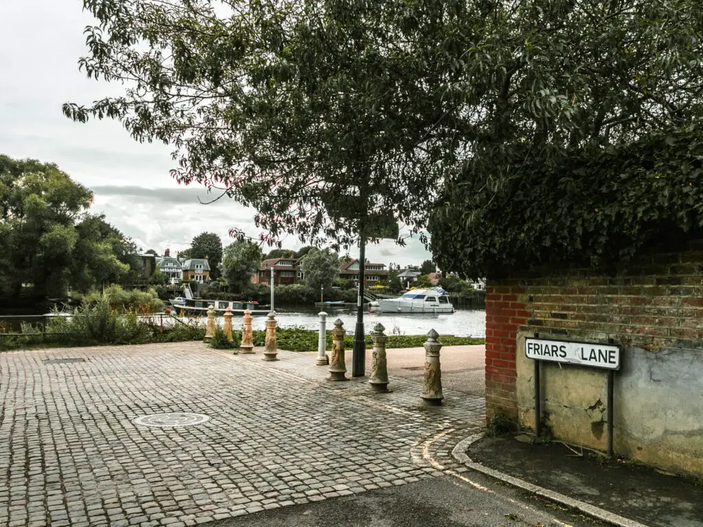 looking onto the Thames Path, with the river head, and a brick wall to the right with a road sign saying 'Friars lane'.