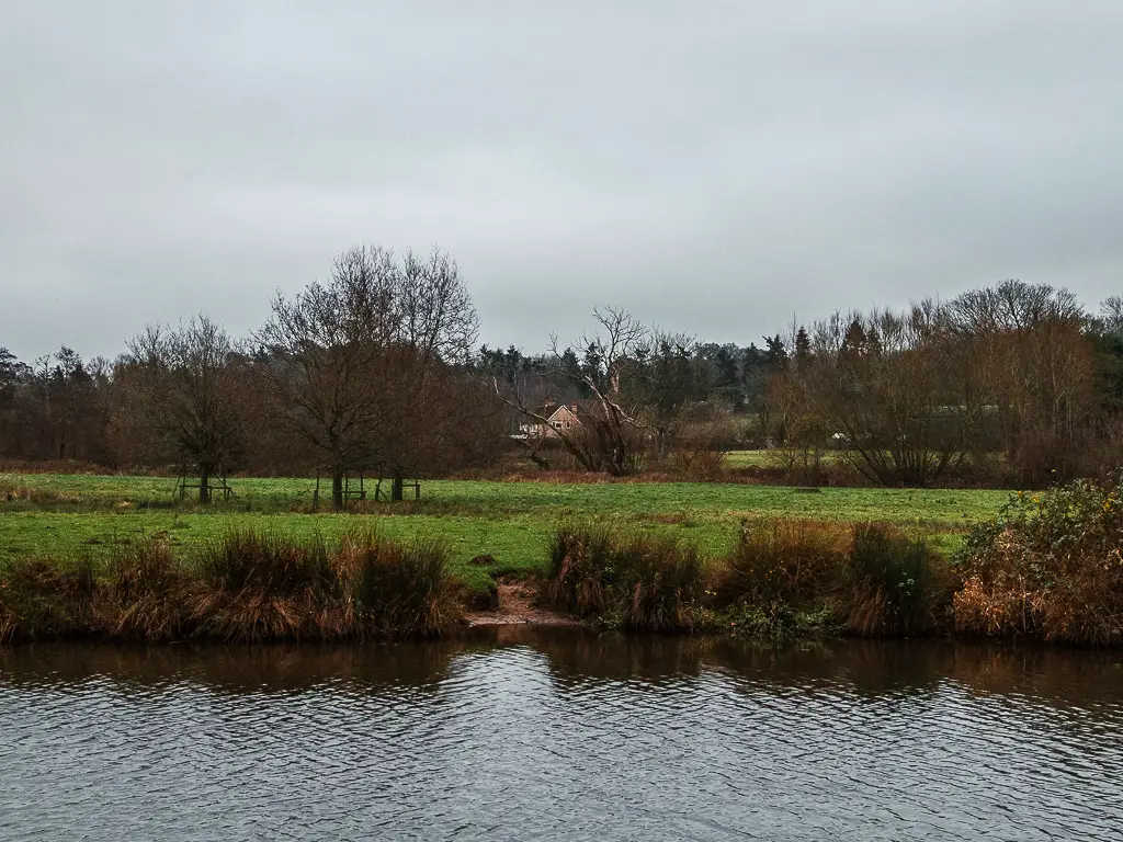 looking across the River Wey, the the field on the other side, on the walk between Godalming and Guildford. The is a house in the field, partially hidden by trees.