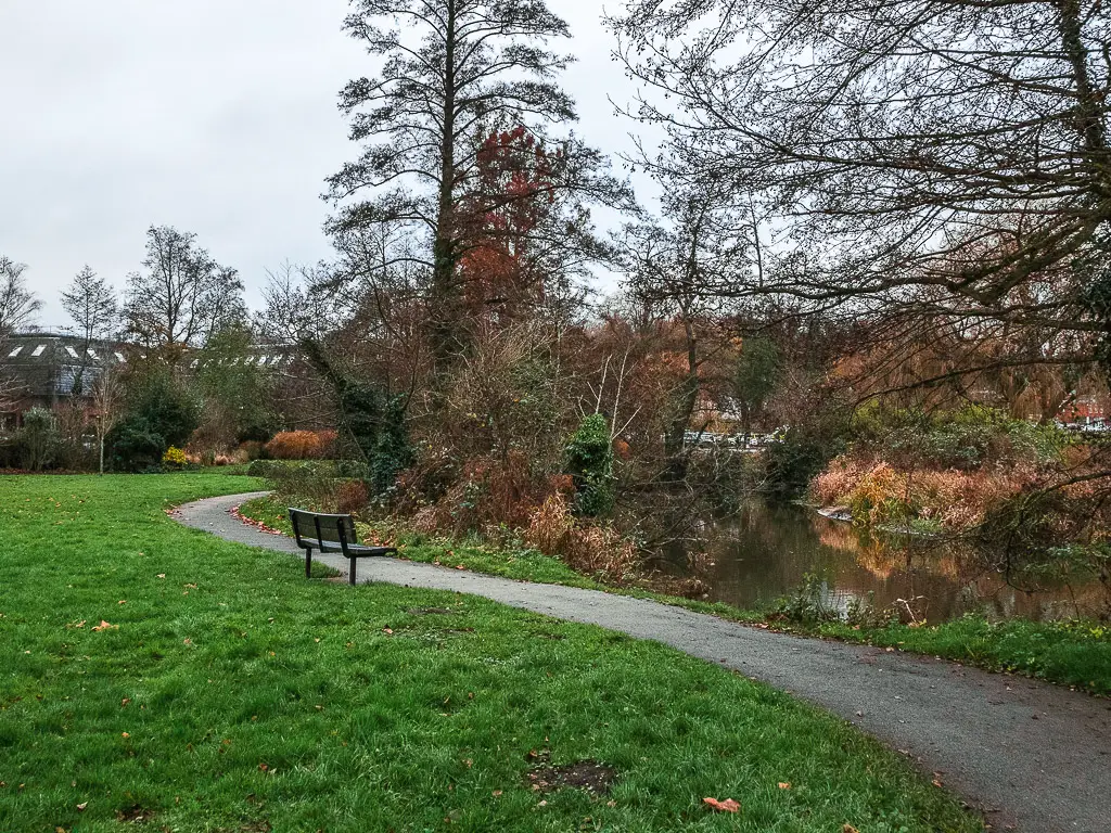 The trail as it snakes around a green. There is a bench on the trail looking to the river.