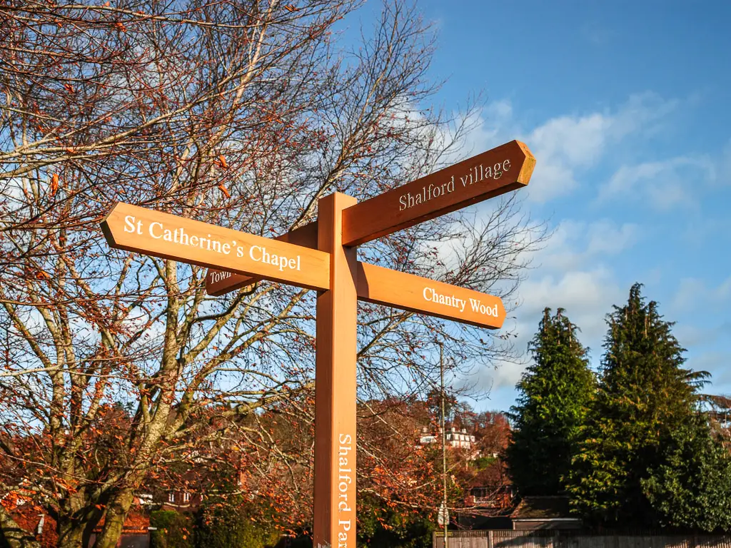 A wooden signpost pointing the way to chantry wood, Shalford village and st Catherine's chapel. 