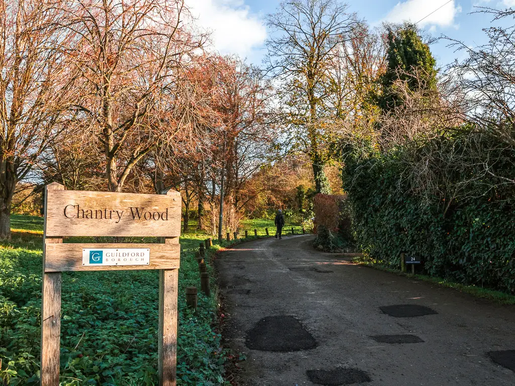 A wooden sign saying 'chantry wood' with a man ahead on a walk up the road. 