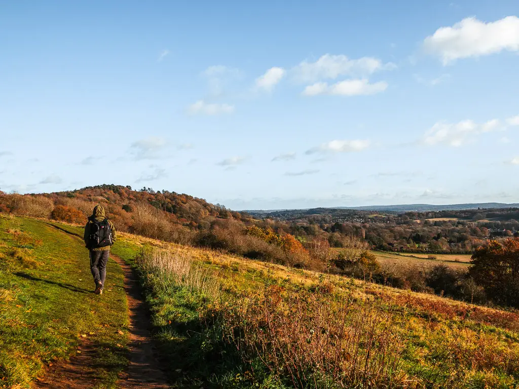 A man walking along a dirt trail on the side of a hill.