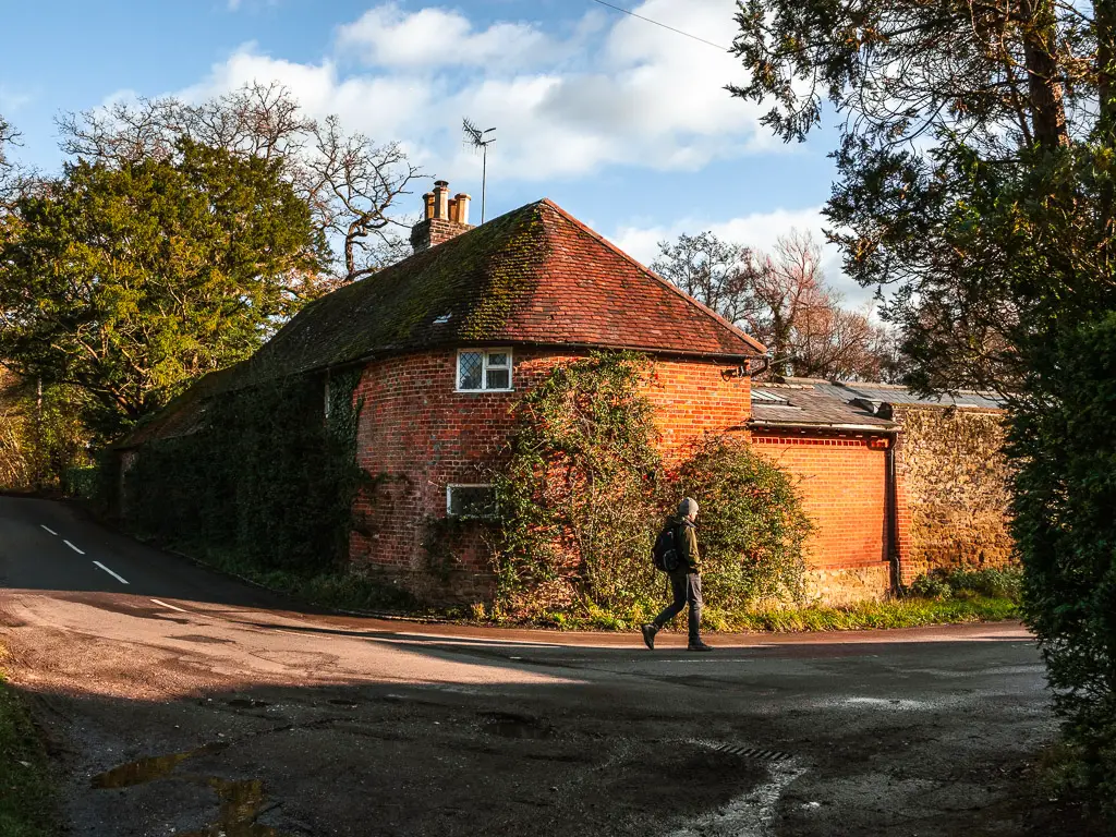 A man walking on a road bend next to a red brick house with curved walls on the walk towards Chilworth Gunpowder mills.