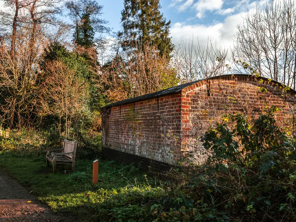 A curved brick hut on the walk through the Chilworth gunpowder mills. There is a wooden bench next to the hut.