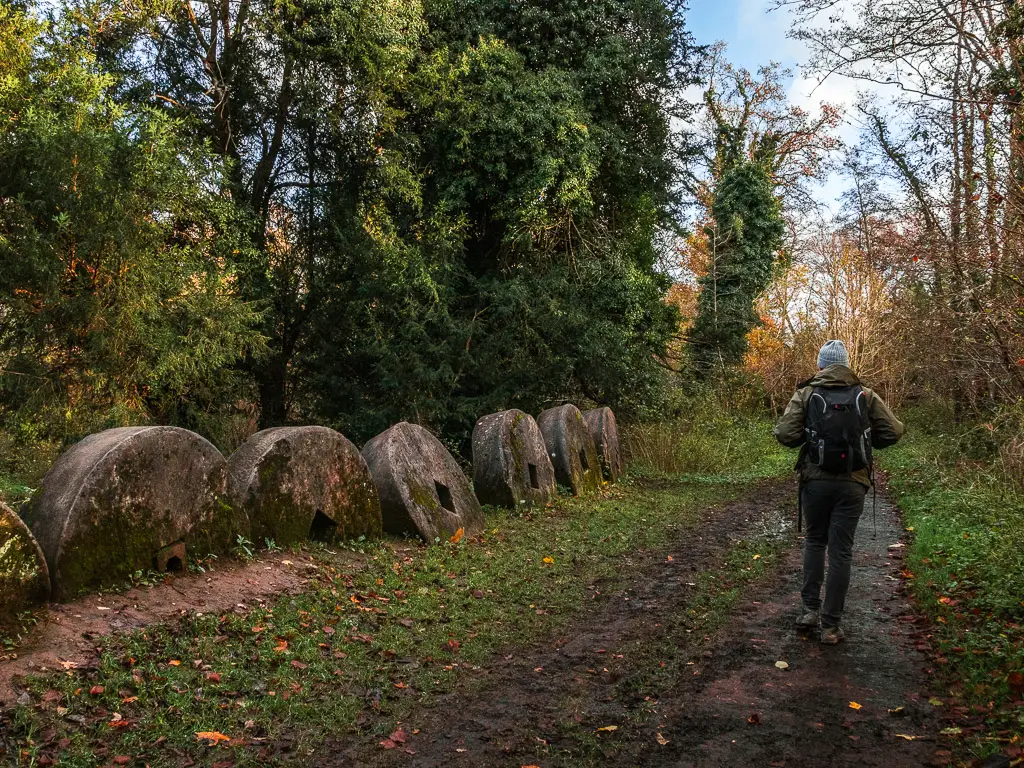 A man on a walk on the dirt path next to a row of edge runner mill stones in the Chilworth Gunpowder mills.