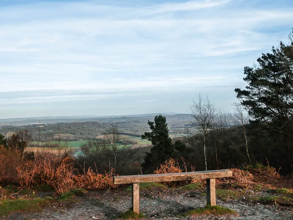 A wooden bench looking out to the view of the green fields and hills on the walk to devil's punch bowl 