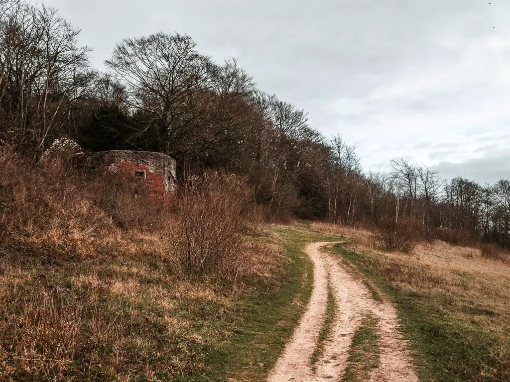 A trail running along the top of a grass hill, with a war pillbox hidden to the left.