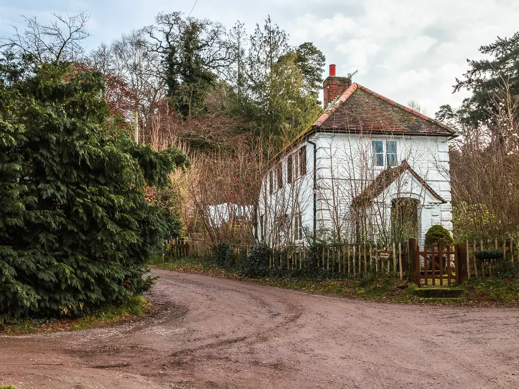 The road leading up the left side of a cute white house on the walk from Guildford to Westhumble. The house is surrounded by a wooden gate.