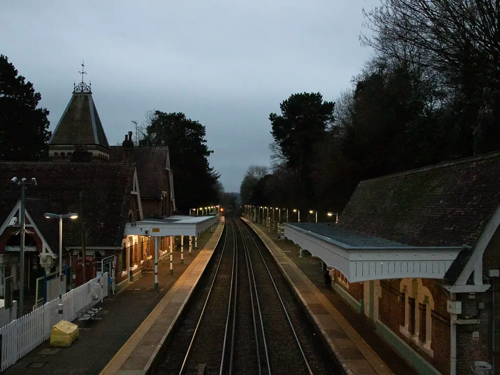Looking down across the train tracks of Westhumble station at night. The lights re on, lining the train tracks along the platform. 