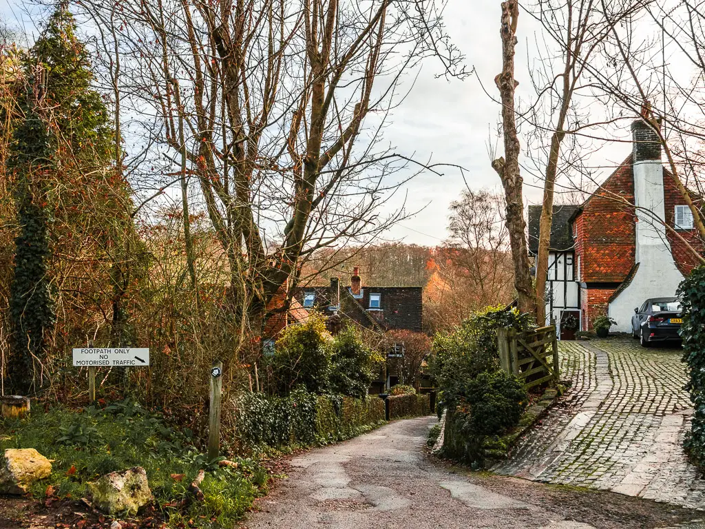 A narrow road leading down hill between the houses at the start of the walk from Guildford to Westhumble. The road is lines with hedges and a brick wall.