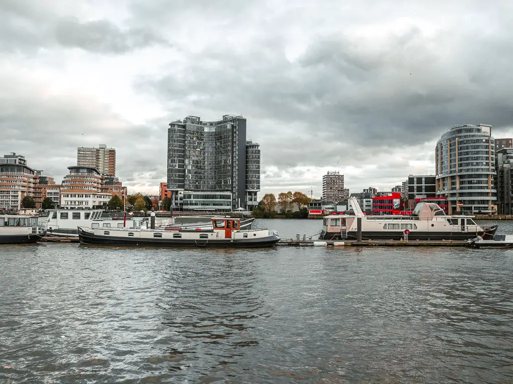 Boats moored in the middle of the River Thames, with tall apartment buildings on the other side.